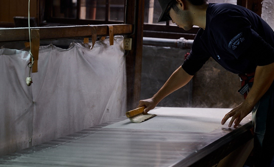 蒸気で熱くなった鉄板の上に１枚１枚和紙を置いて乾燥させる工程
